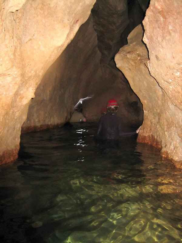 A person wearing a red helmet explores an underground cave pool surrounded by rocky walls.