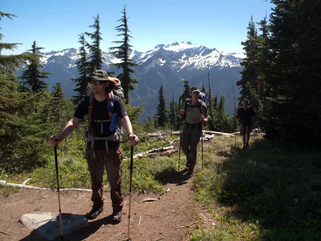 Hikers on a dirt trail with forest and mountain views in the background.