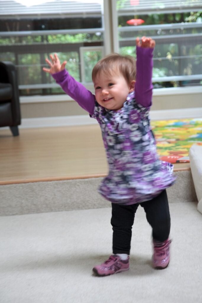 Tot in a purple floral dress plays joyfully in a bright living room.