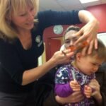 A young child getting their hair braided by an adult in a home setting.