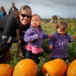 A woman and two toddlers enjoy picking pumpkins at a farm in the Pacific Northwest.