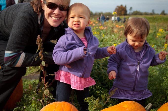 A woman and two toddlers enjoy picking pumpkins at a farm in the Pacific Northwest.