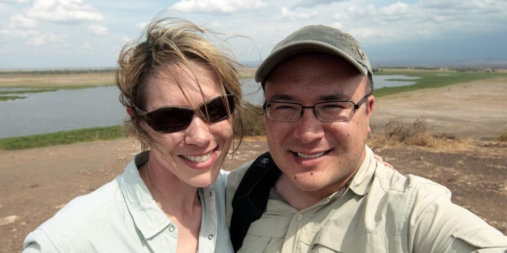 Three people smile for a group and individual selfie by the water in a flat landscape.