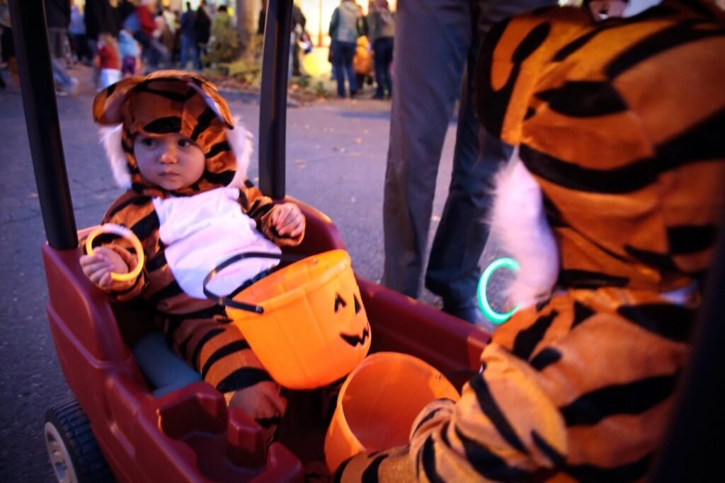 A child and adult dressed in tiger costumes riding a wagon at a Halloween event with trick-or-treat buckets.