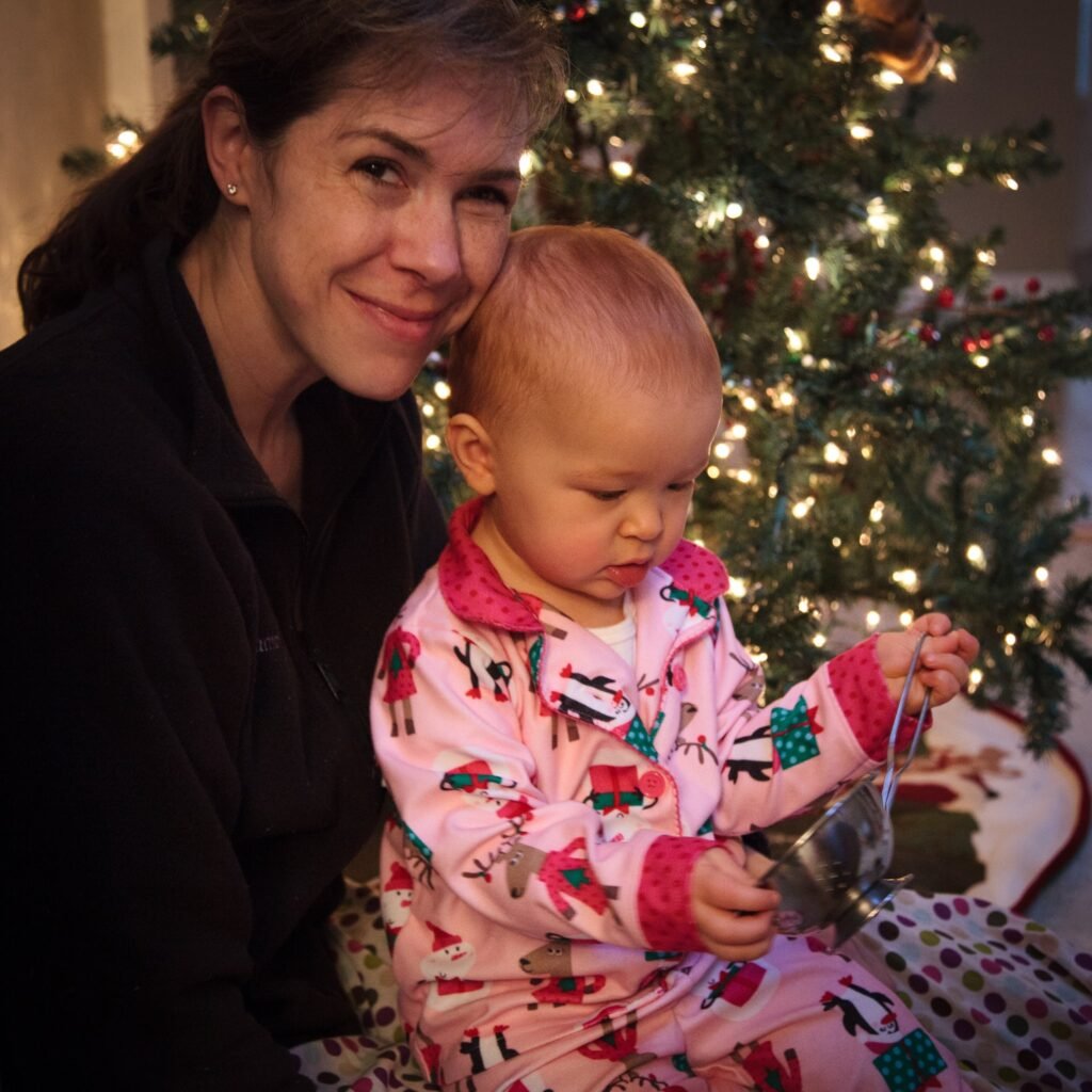 Woman and toddler in Christmas pajamas by a lit tree; warm indoor holiday scene