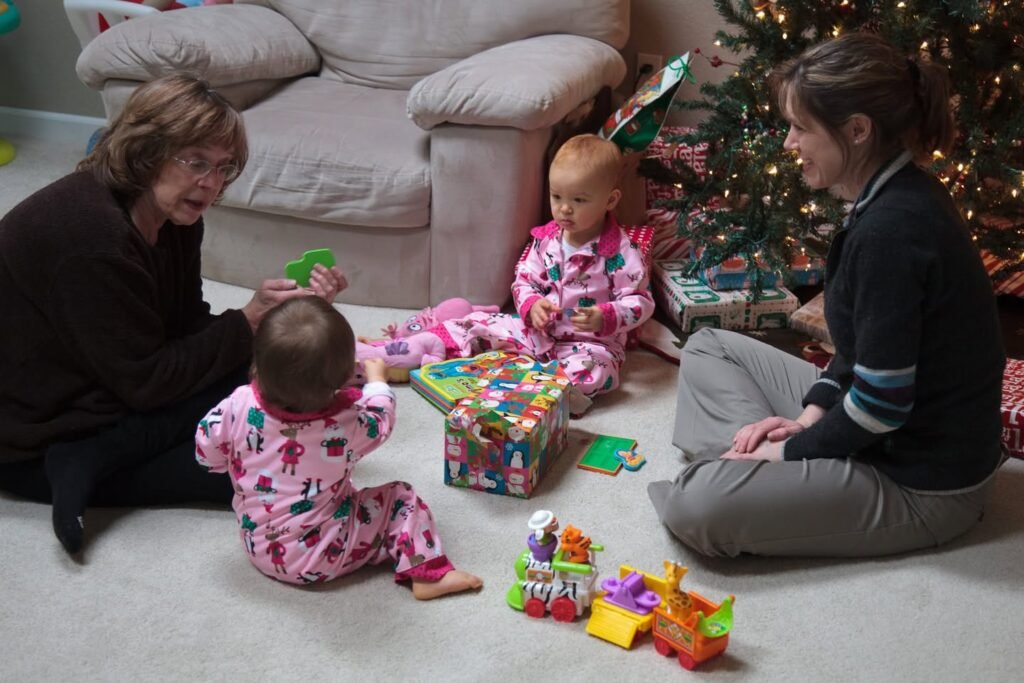 A family enjoys opening gifts together in a cozy living room with a decorated Christmas tree in the background.