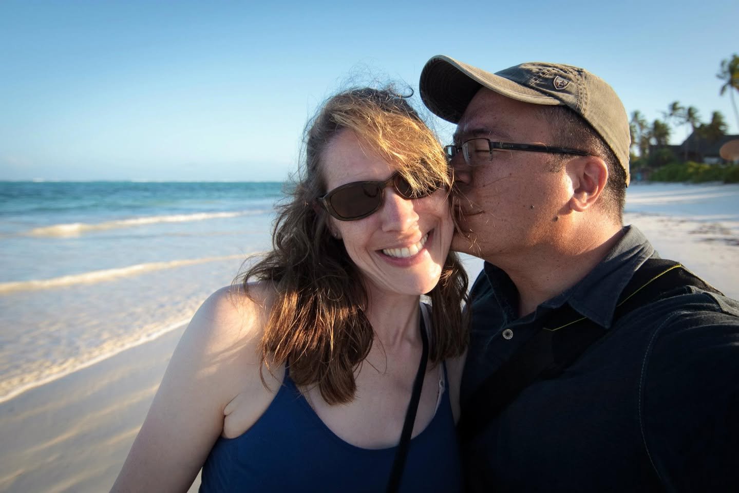 Safari: Part 3 of 3 Two people posing for a photo at the beach on a sunny day. Gentle waves and a clear blue sky in the background.