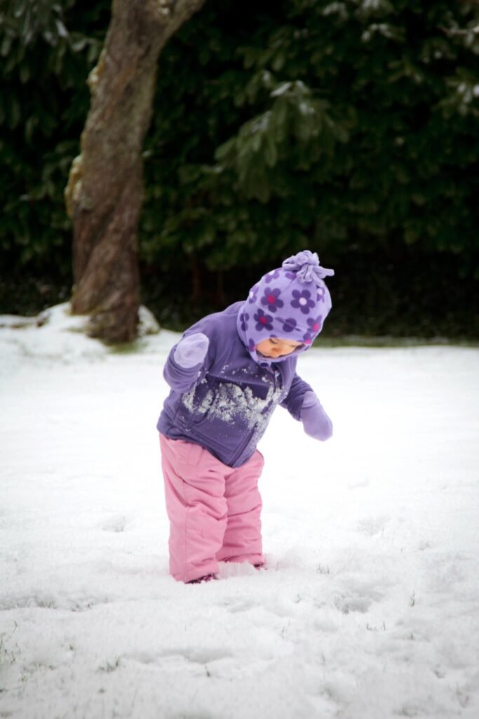 A cute little one bundled in a purple jacket and pink snow pants explores the snow. A delightful moment captured during a winter day in the Pacific Northwest.
