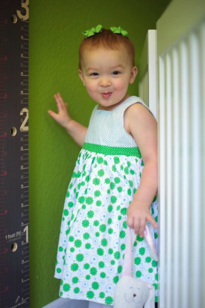 Toddler standing against a green wall in a matching polka dot dress with a clip in hair.