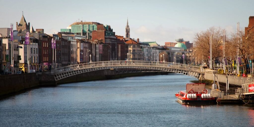 A scenic view of the Nyhavn canal in Copenhagen featuring colorful buildings and a pedestrian bridge. The serene water reflects the historic architecture.