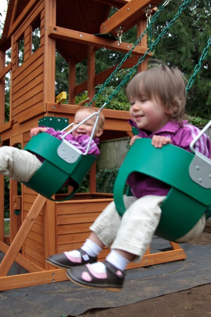 Two kids enjoying a swing on a wooden playset, making the most of a sunny afternoon.