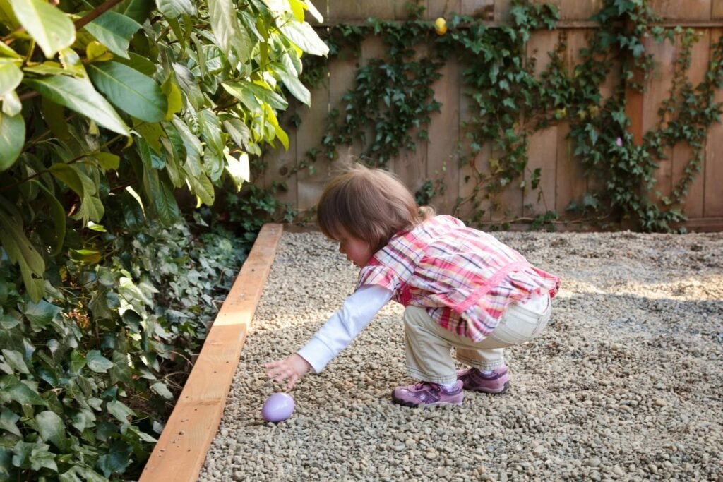 A child in a garden surrounded by green leaves and a wooden fence.
