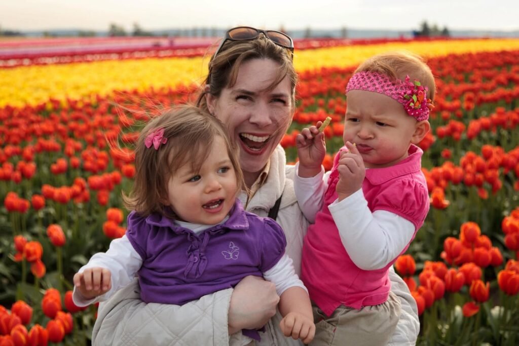 A woman holds two young children amidst vibrant red and yellow tulips in a scenic flower field.