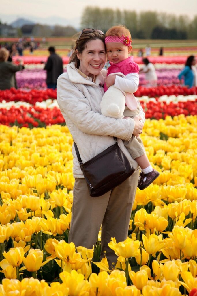 Photograph of a family standing in a field of vibrant yellow and red tulips with mountains in the distance on a sunny day.