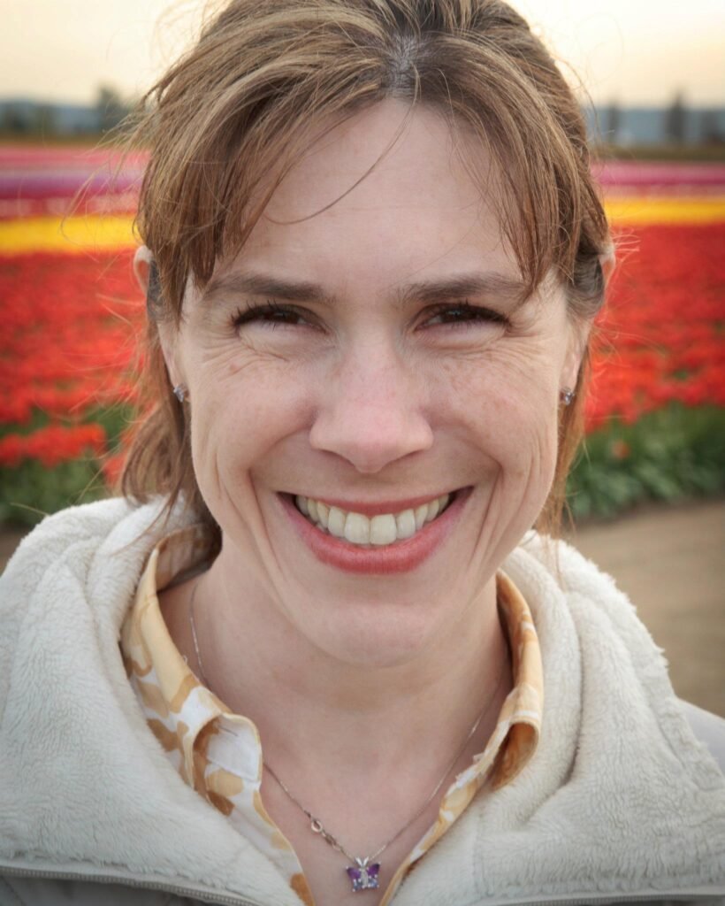 A smiling person stands in front of vibrant, colorful flower beds at a tulip farm.