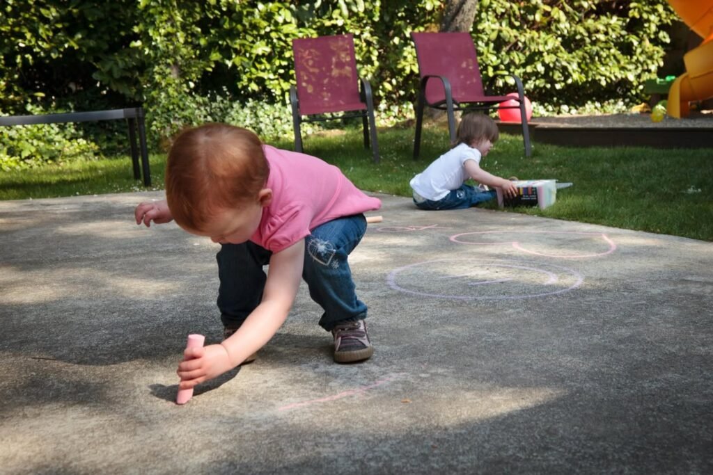 Children drawing with chalk on a concrete surface at a sunny outdoor park.