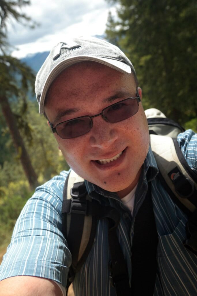 Selfie of a hiker in a forest setting. Another hiker is visible in the close-up shot.