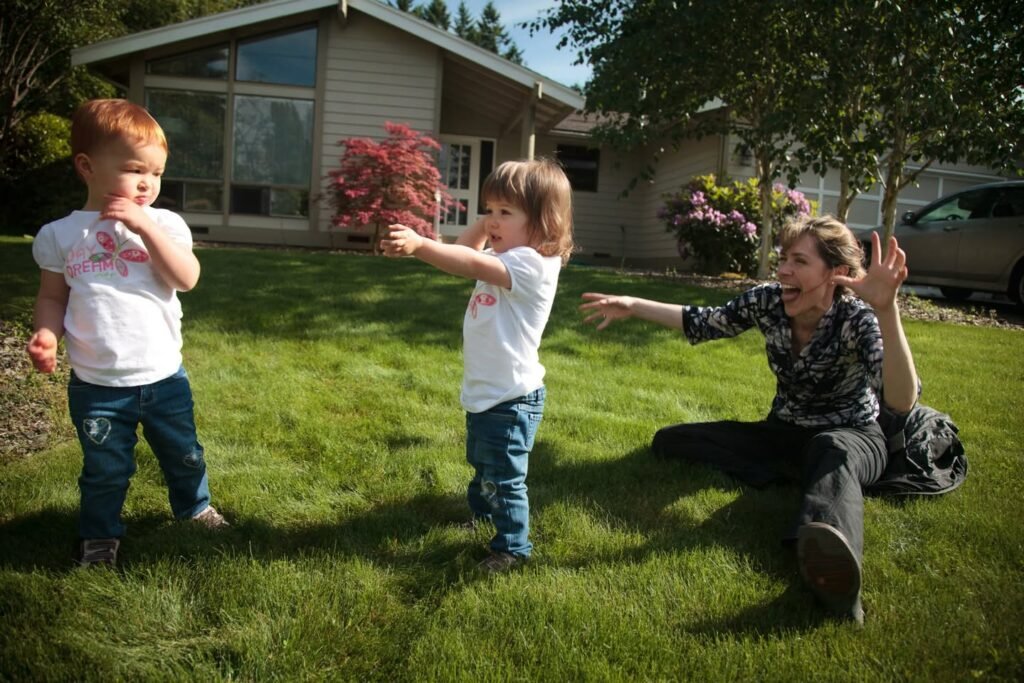 A child and adult playing on a grassy backyard lawn near a house.