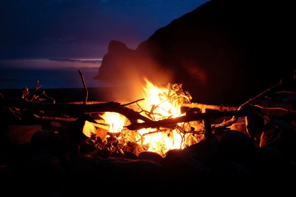 A bright campfire burning against a twilight sky in a coastal setting.