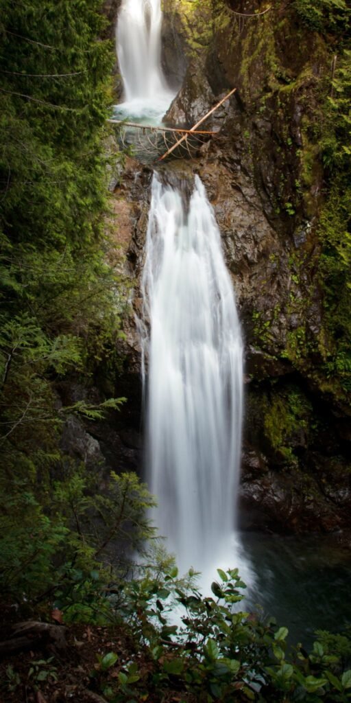 A serene waterfall cascades over a rocky cliff face into a pool of clear water, framed by lush vegetation.
