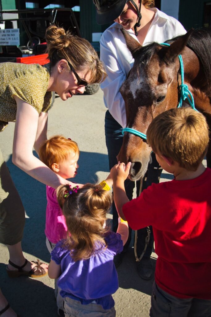 A group of children are seen gently touching and interacting with a brown pony with a blonde mane, supervised by adults.