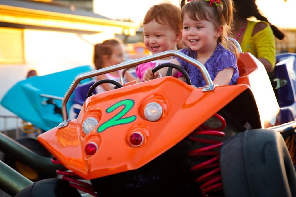 Children ride brightly colored kiddie karts at a carnival event, smiling as they enjoy the spinning ride.