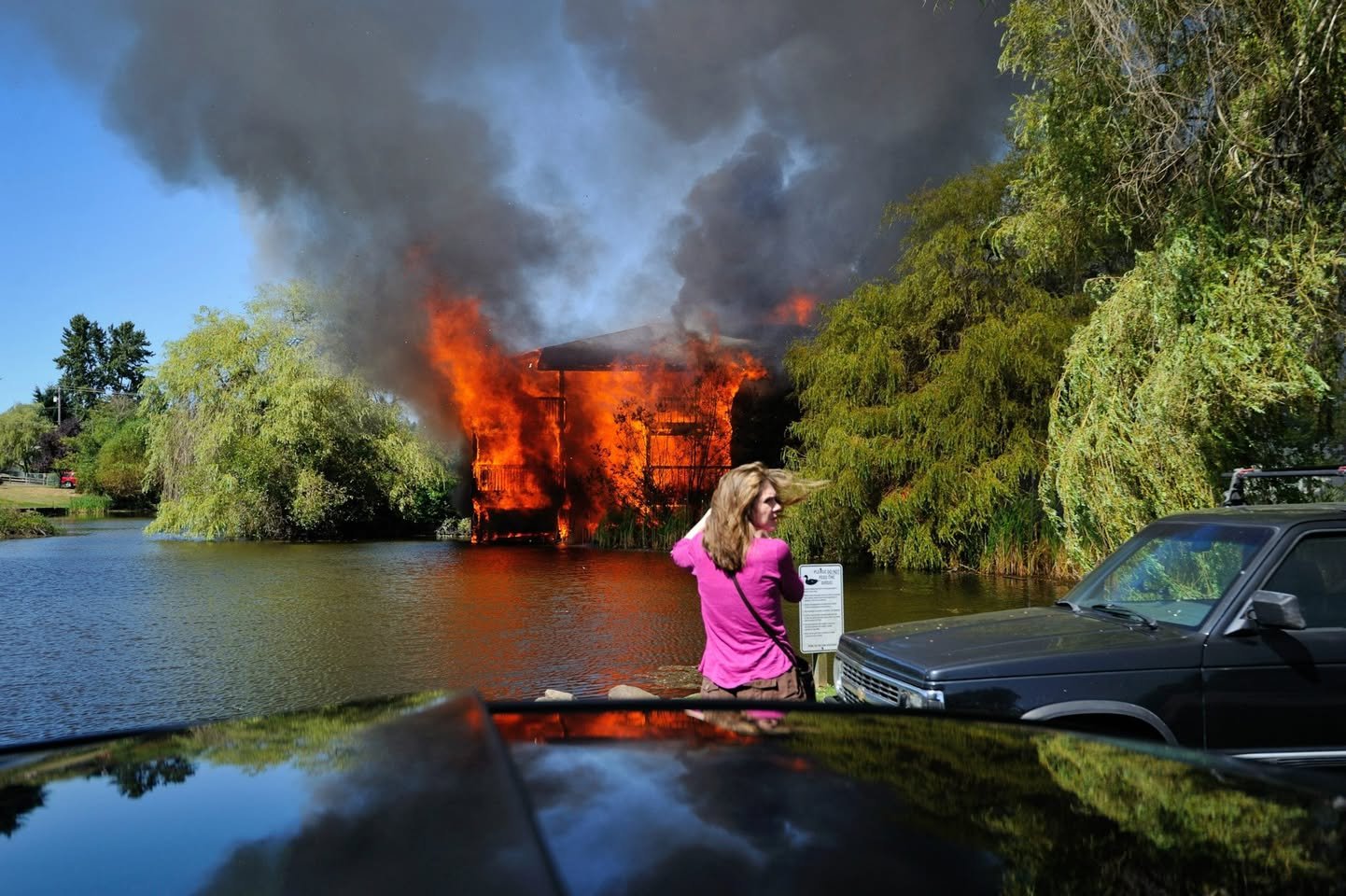 Office Fire A striking scene of a burning car with intense flames and dark smoke rising from a green shoreline.