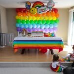 A child-friendly birthday party space decorated with a rainbow balloon wall and themed table setting.