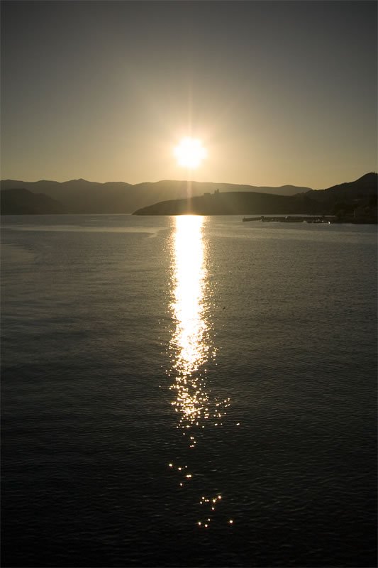 A serene sunset over a calm body of water, with distant mountains silhouetted against the horizon.