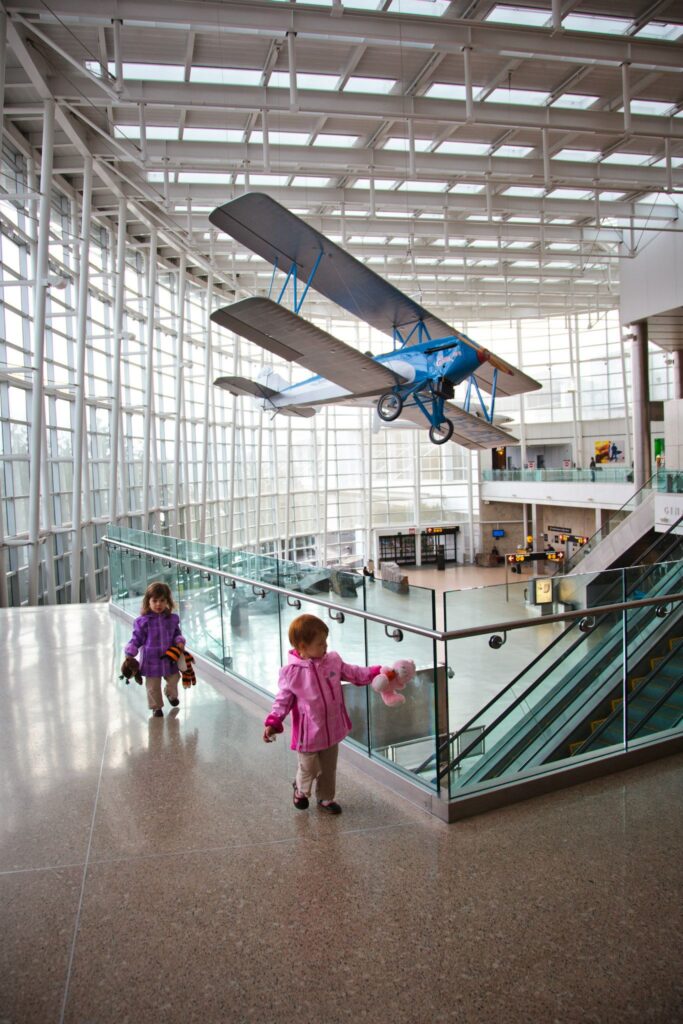 Two children explore the expansive interior of the Boeing Factory complex while a vintage aircraft hangs from the suspended ceiling.