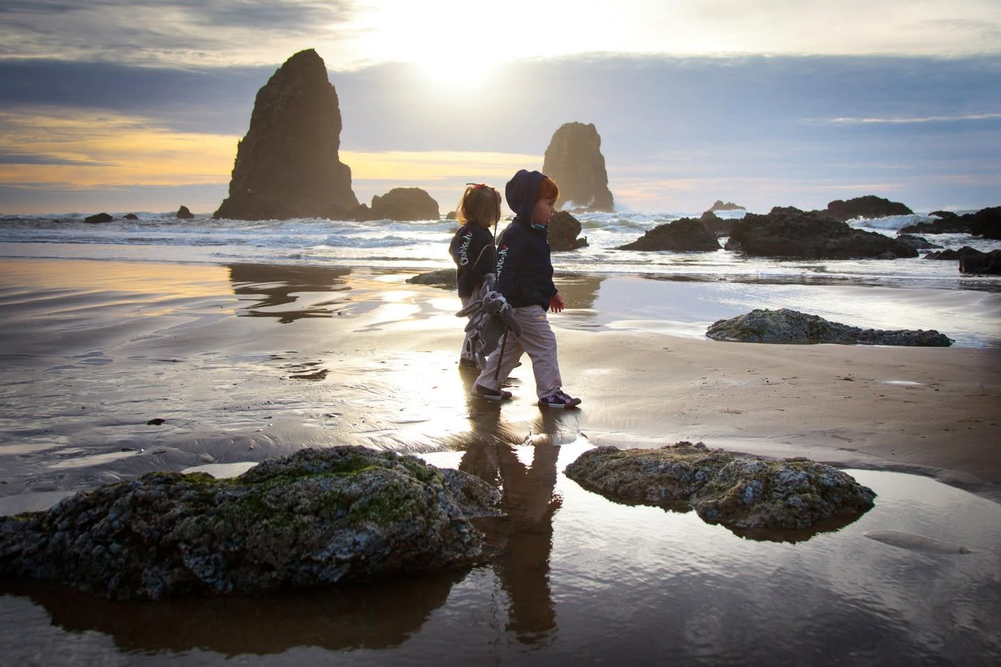 Thanksgiving at Cannon Beach Two people walking on a wet sandy beach with prominent sea stacks and their reflections at sunset.