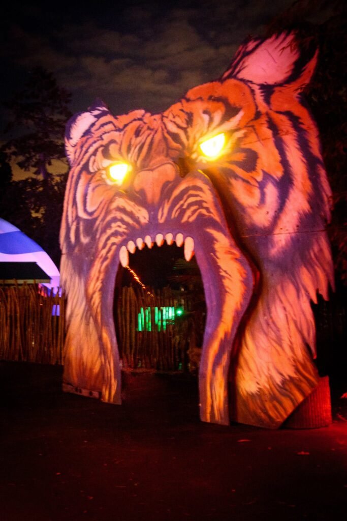 A glowing illuminated tigon archway with eyes and teeth lit at night. This light structure highlights striped patterns against a dark sky.