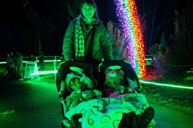 Vibrant rainbow LED lights arching over a path at night illuminating a stroller in green glow.