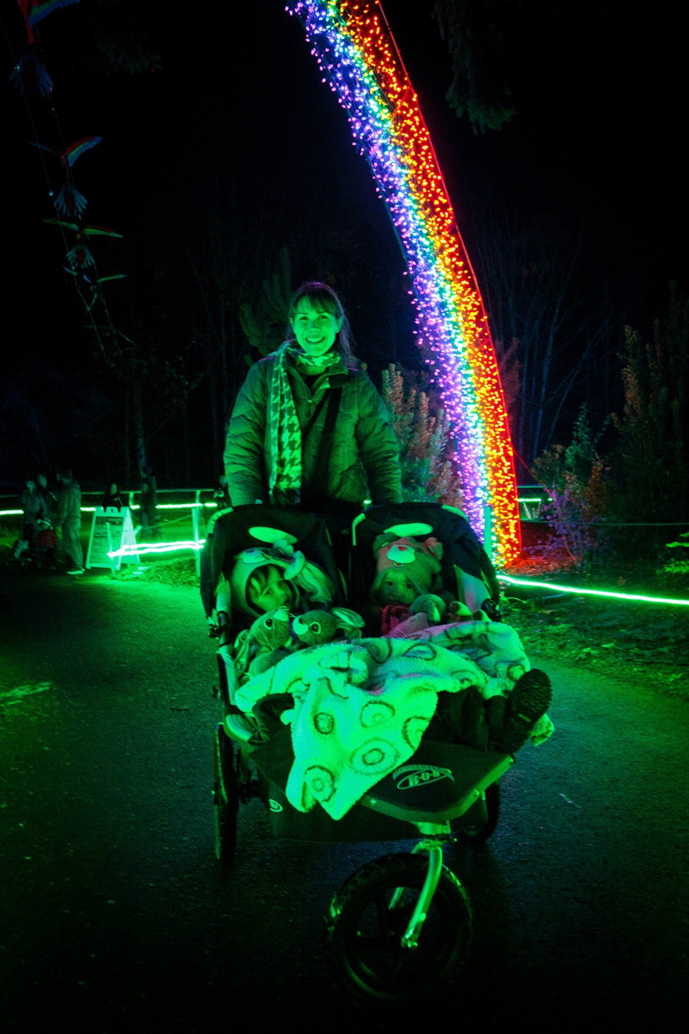 Zoolights Vibrant rainbow LED lights arching over a path at night illuminating a stroller in green glow.