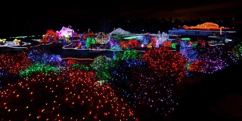 A nighttime aerial view of a sprawling Christmas light show featuring colorful lights on houses and trees in the Pacific Northwest.