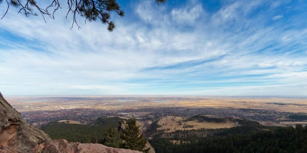 A panoramic view of vast landscape from a mountain peak with scattered clouds.