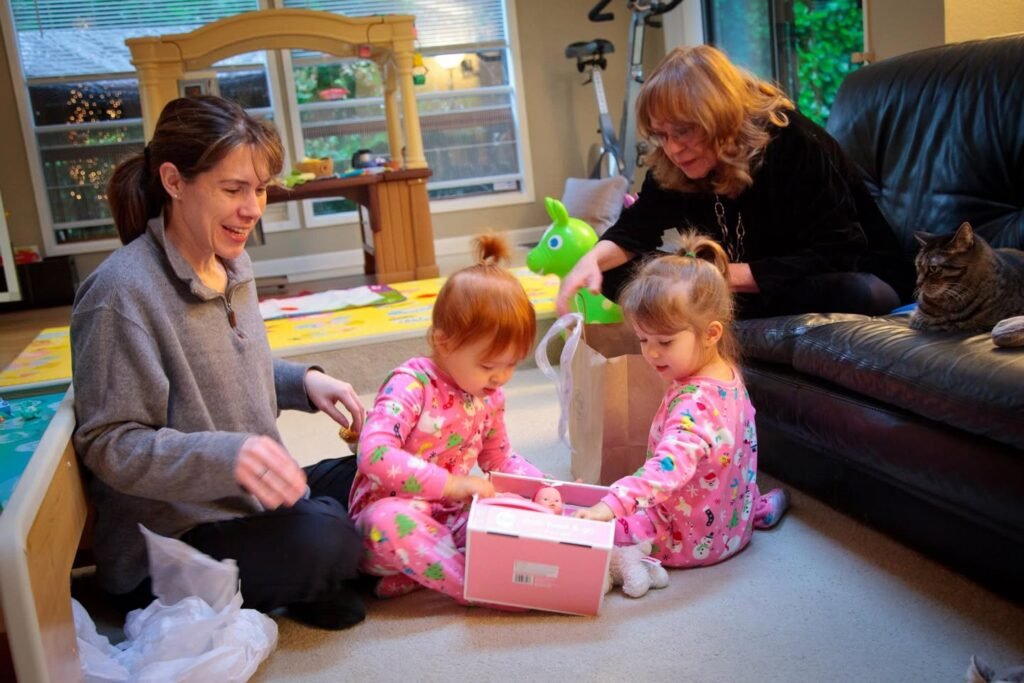 A family is gathered in their home while two children open a pink gift box on the floor.