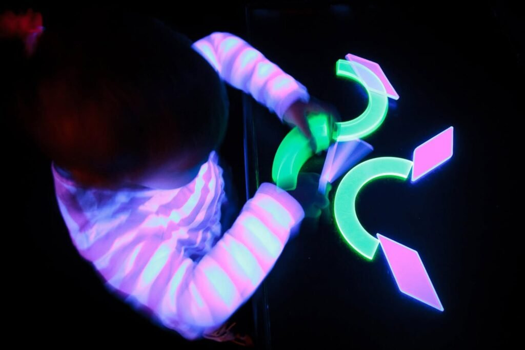 Person in striped shirt under blacklight interacting with glowing geometric shapes.