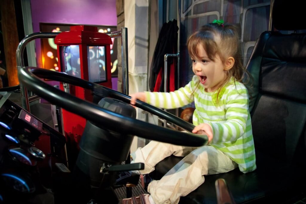 A toddler in a green striped shirt plays happily with a large black wheel indoors.