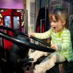 A toddler in a green striped shirt plays happily with a large black wheel indoors.