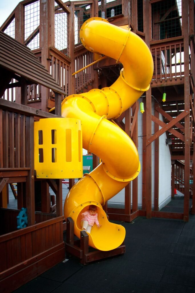A bright yellow spiral tube slide connects multiple levels of a large wooden play structure.