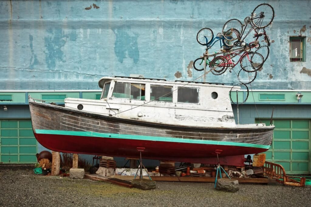 A weathered fishing boat rests on wooden supports with a metal sculpture of bicycles mounted above its cabin.
