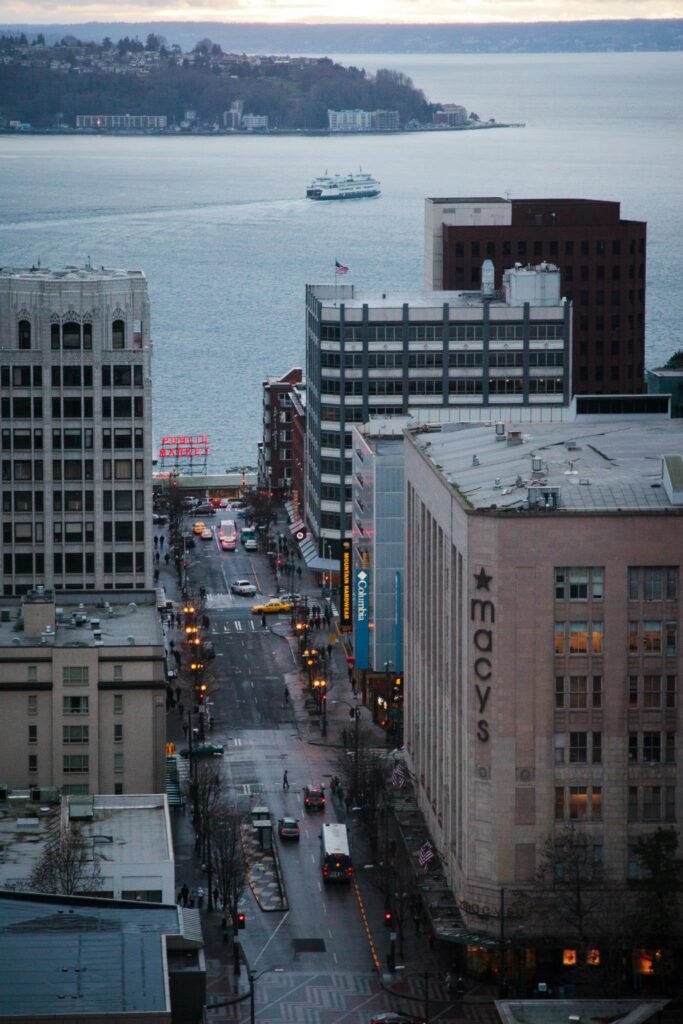 A high-angle view of downtown Seattle buildings with the Moxy hotel and Puget Sound in the background.