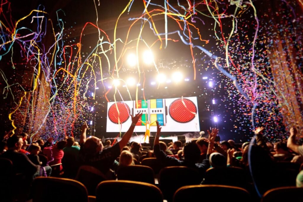 A massive crowd cheering with arms raised as colorful fireworks explode over a stadium during a New Year's Eve countdown.