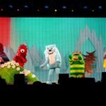Colorful puppets from the Polar Express appear on a stage with a snowy backdrop in Portland, Oregon.