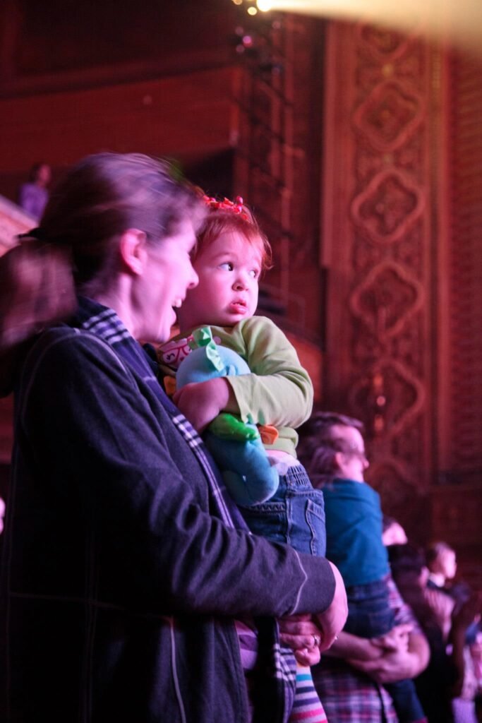 A person shares a special moment while holding a child during a performance in a warmly lit theater.