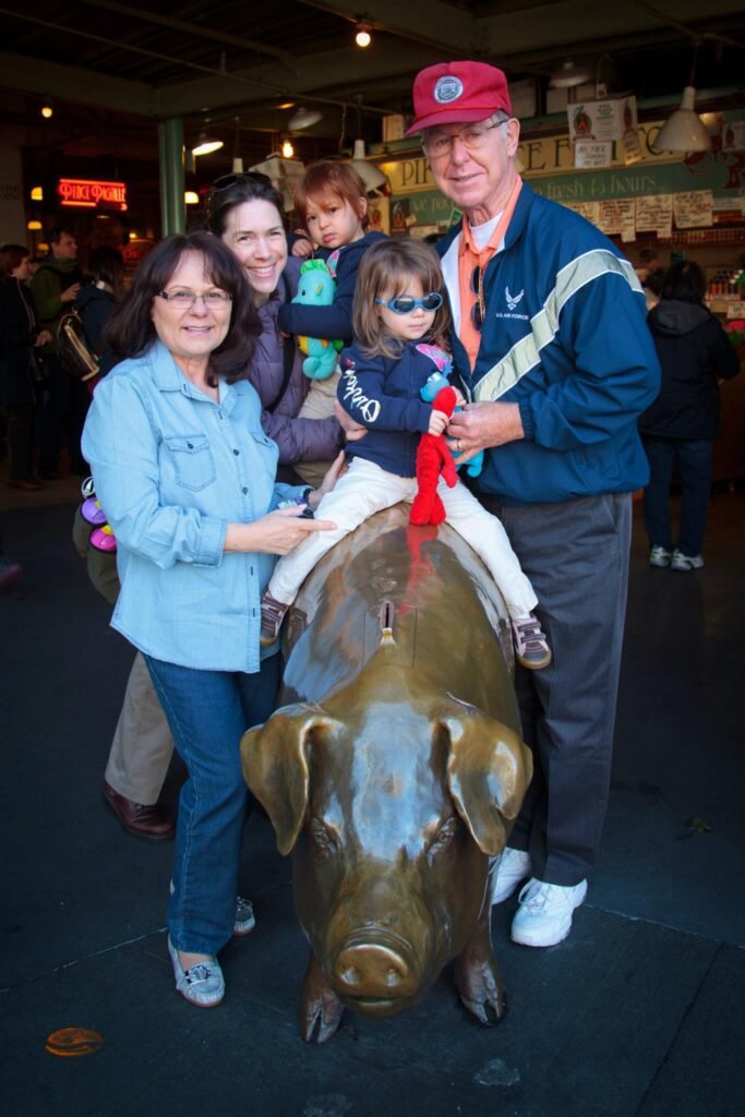 A family poses with a young child on a large pig statue in a public market setting.