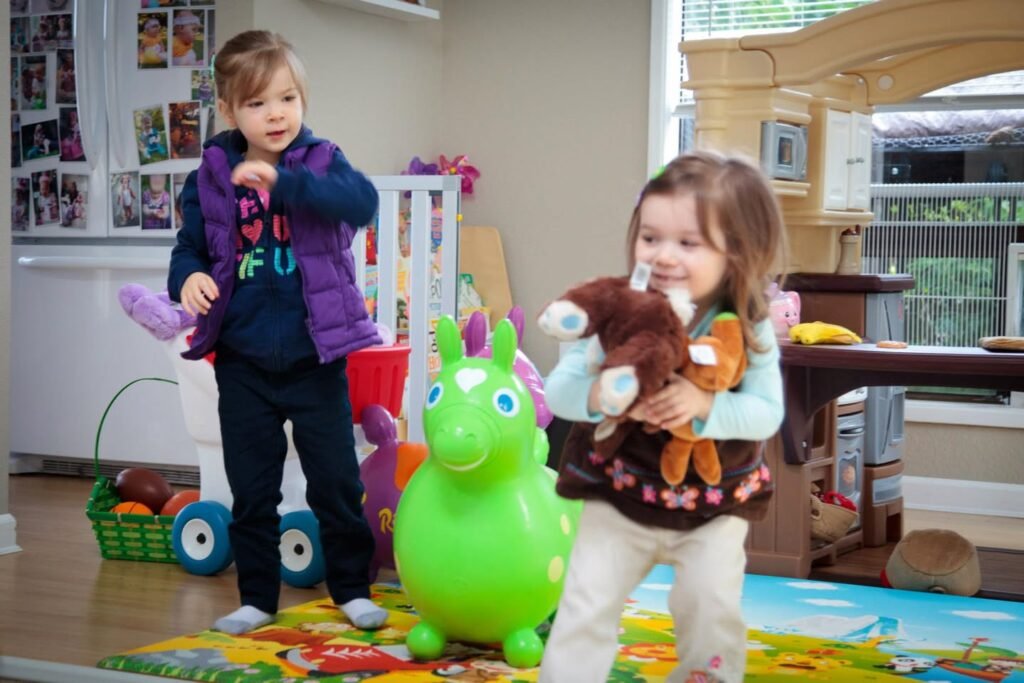 Two children playing with toys, including a green inflatable animal and a stuffed toy.