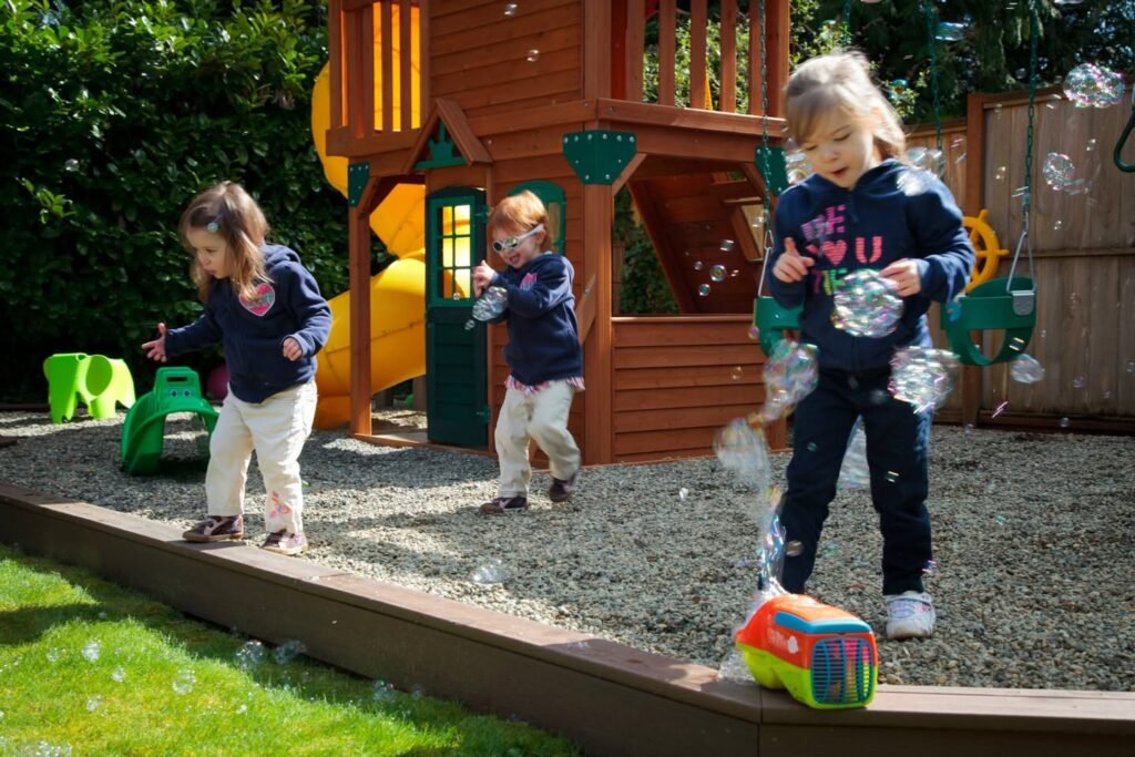 Children playing with bubbles in a backyard featuring a wooden playset.