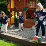 Children playing with bubbles in a backyard featuring a wooden playset.